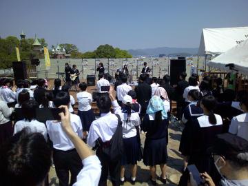 ステージの上で高校生バンドが歌を披露し、聴衆が集まっている様子