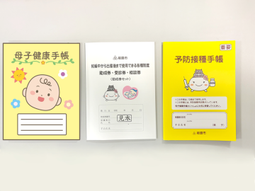 母子健康手帳のイメージ画像と、助成券セットと、予防接種手帳を並べて撮影した画像