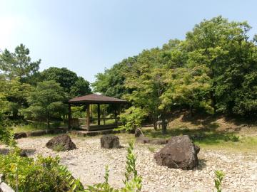 木々に囲まれた屋根付きの東屋が立つ晴れた日の風景