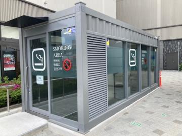 戸外の歩道脇に設置されたガラスと金属で囲まれた喫煙所の小屋