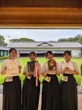 選手の生徒4人が各自表彰状やトロフィーを持って道場内で記念撮影の様子