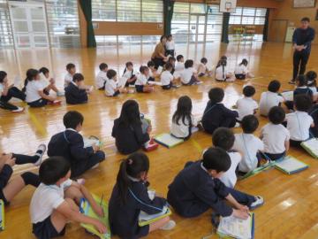 体育館で学校たんけんはじめのあいさつを聴く児童の様子