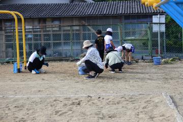 運動場の草引きをする保護者の方と子供達