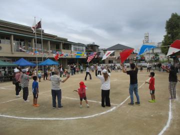 園庭で園児と保護者が全員で円になってダンスを踊る様子