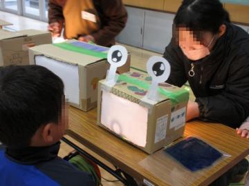 目をつけた段ボールの箱の向こう側から光を当てて何のシルエットを映しているか当てようとしている生徒