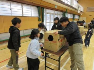 側面に穴の開いた段ボール箱に手を入れて触感だけで何が入っているかを当てるゲームをしている生徒