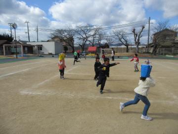 運動場で鬼を追いかけ、豆まきをしている園児たちの様子