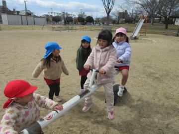 園庭で、3歳、4歳、5歳児がシーソーに乗っている様子