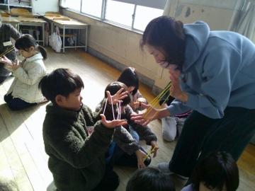 児童が老人クラブの方にあやとりを教えてもらっている写真