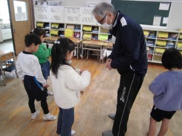 児童がけん玉のひもの巻き方を老人クラブの方に教えてもらっている写真