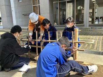 屋外で生徒が熟練技能者から四ツ目垣づくりの指導を受けている様子