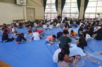 体育館の床にブルーシートを敷いて、そのうえで生徒達が陶芸教室をしている様子