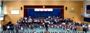 体育館の壇上に立って並ぶ生徒とその前に楽器と一緒に並ぶ生徒の音楽会全体の写真
