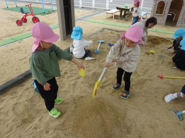 砂場で、友達と協力して大きな山を作る園児の様子