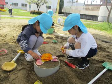 砂のケーキに花びらをのせて遊ぶ子供