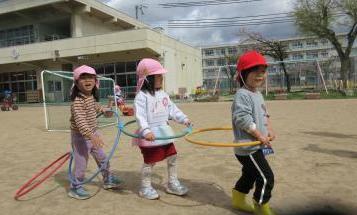 園庭で園児がフープをつないで電車ごっこをしているところ