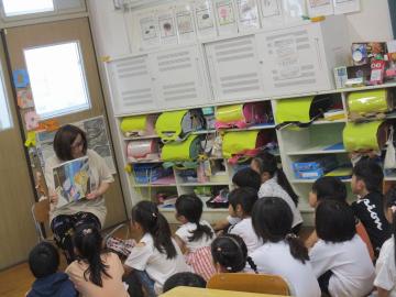 教室の後ろに集まって、床に座って絵本を読んでもらっています