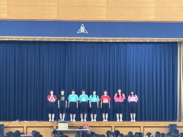 体育館の壇上で女子卓球部の代表生徒が挨拶する様子