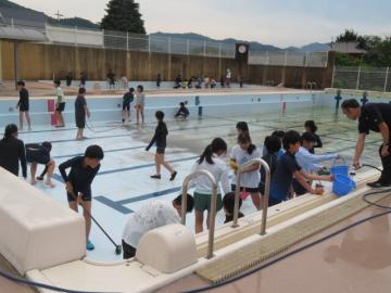 バケツに水をくみ流しながらプールをみがく6年生