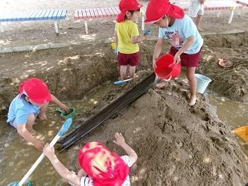 砂場で樋を使って遊んでいる写真