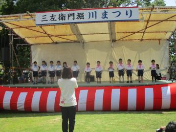 川まつりの舞台で歌を歌う子供たち