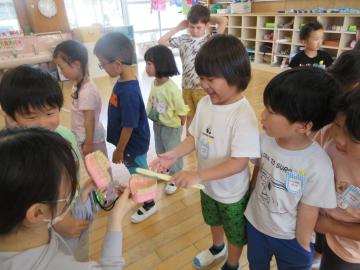 園内で園児が歯の模型を使い、歯を磨く画像