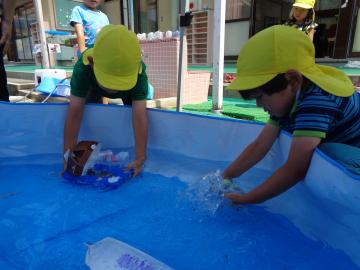 園児が園庭で手作りの船を水に浮かべている様子