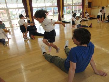 園児が遊戯室内でお家の人の足の上をジャンプしている様子