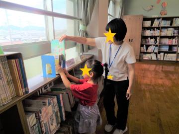 司書の先生に探している絵本の場所を教えてもらっている子ども
