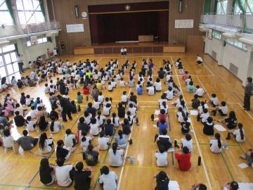 体育館で、集会委員会の代表が全校集会のはじめの言葉を述べている様子