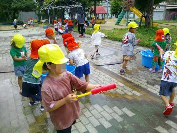 園児が園庭内で水鉄砲で遊んでいる様子