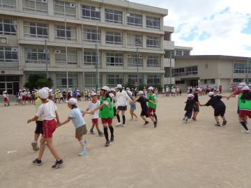 全校ダンスです。児童が運動場で手をつないで踊っています。