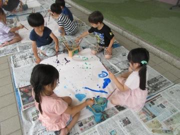 園児が模造紙を囲んで座り絵の具で雨をかいています