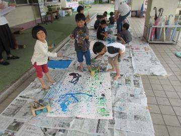 園児が模造紙に向かって絵の具のついた筆を振る場面