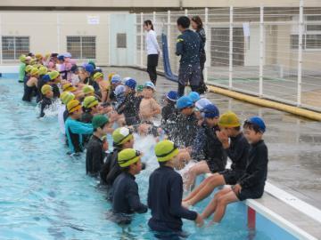 学校水泳において、プールに入った6年生の児童たちがプールサイドに腰かけた1年生の児童たちを補助している様子