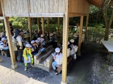 国見の森の中で、動物の話を指導員さんから聞いている児童たちの様子