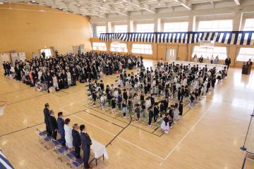 新入生と保護者が整列した椅子の前で起立している風景