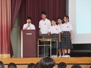 体育館の壇上でスライドを担当ごとに説明する生徒の様子