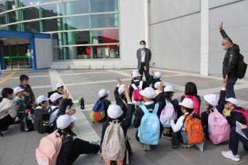 科学館の入り口付近で館長の話を聴く児童たちの様子