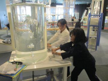 科学館内で友達と協力して水に空気を送り込む児童たちの様子