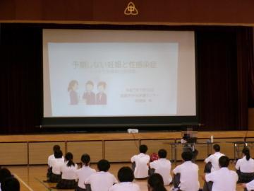 体育館で生徒が整列して座りながら、姫路市中央保健センターの講師先生のお話を真剣に聞いています。