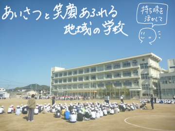英賀保小学校全景と青空、校庭で座る児童たちの画像