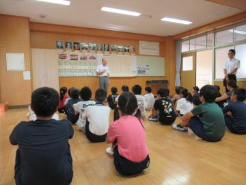 教室に座って校長先生の話を聞いている児童たちの後ろ姿