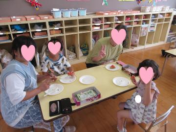 室内でスイカを祖父母と園児たちが食べている様子