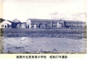 昭和27年の英賀保小学校の写真。田畑向こうに木造校舎が見えます。