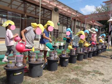 幼児が一列になって自分の植木鉢に水やりをしているところ。
