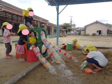 砂場で4歳児数名が手作りのスライダーを使って水遊びをしているところ
