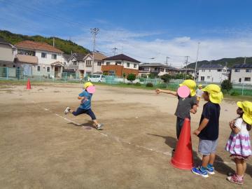 4歳児がリレー遊びをして、友達にバトンを渡そうとしているところ