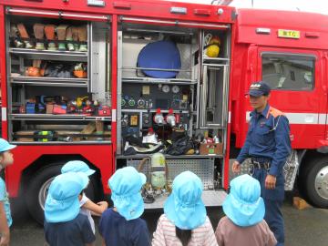 幼児が消防車の中の物を見て、消防士の方に説明をしてもらっているところ