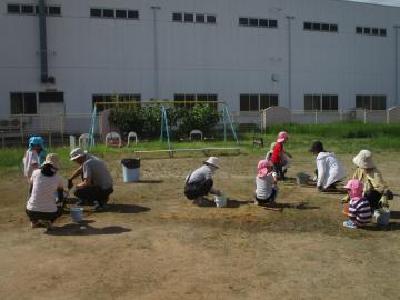 園庭の草抜きをする園児と保護者
